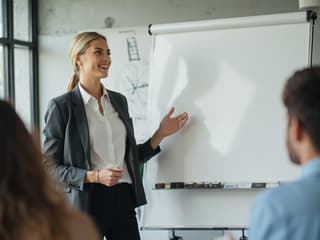 Confident person leading a meeting, gesturing towards a whiteboard