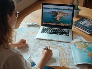 Person planning a trip with maps, guidebooks, and a laptop showing travel websites