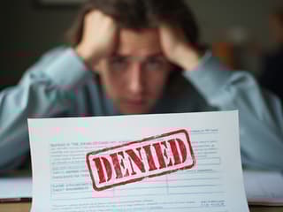 Studio shot of insurance claim documents with denied stamp, person looking frustrated